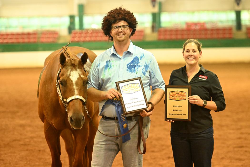 Man with plaque and blue ribbon beside horse; woman holding plaque reading "Champion 4‑H Alumni"
