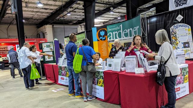 Booth for "Successful Gardener" with staff advising visitors at an indoor fair