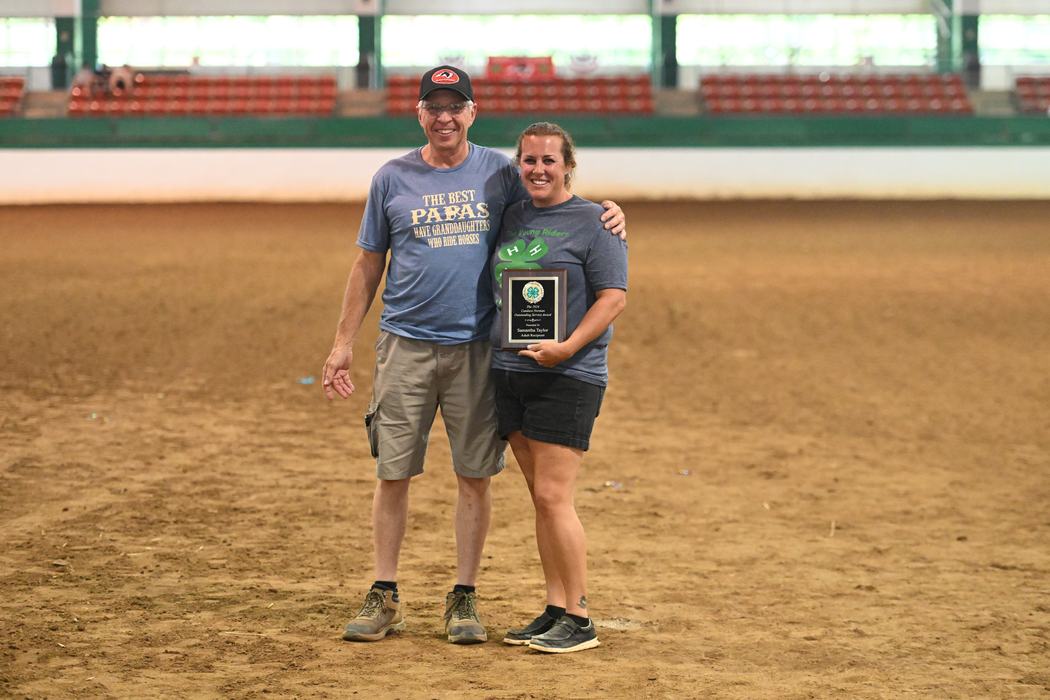 Man and woman standing in an arena, woman holding a plaque award.