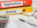 Red binder labeled "Applications" atop yellow binder labeled "Grants" on desk