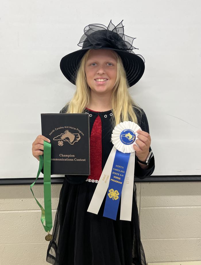 Girl in black hat holding Champion Communications plaque and North Carolina 4‑H Horse ribbon