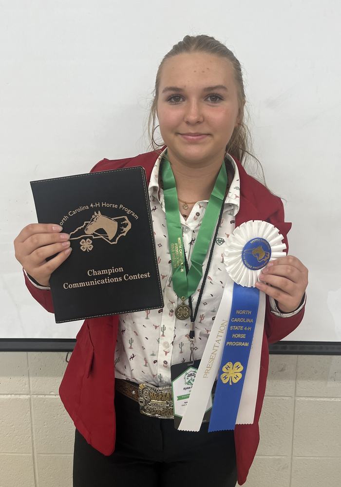 Young person holding "Champion Communications Contest" plaque and 4‑H Horse ribbon