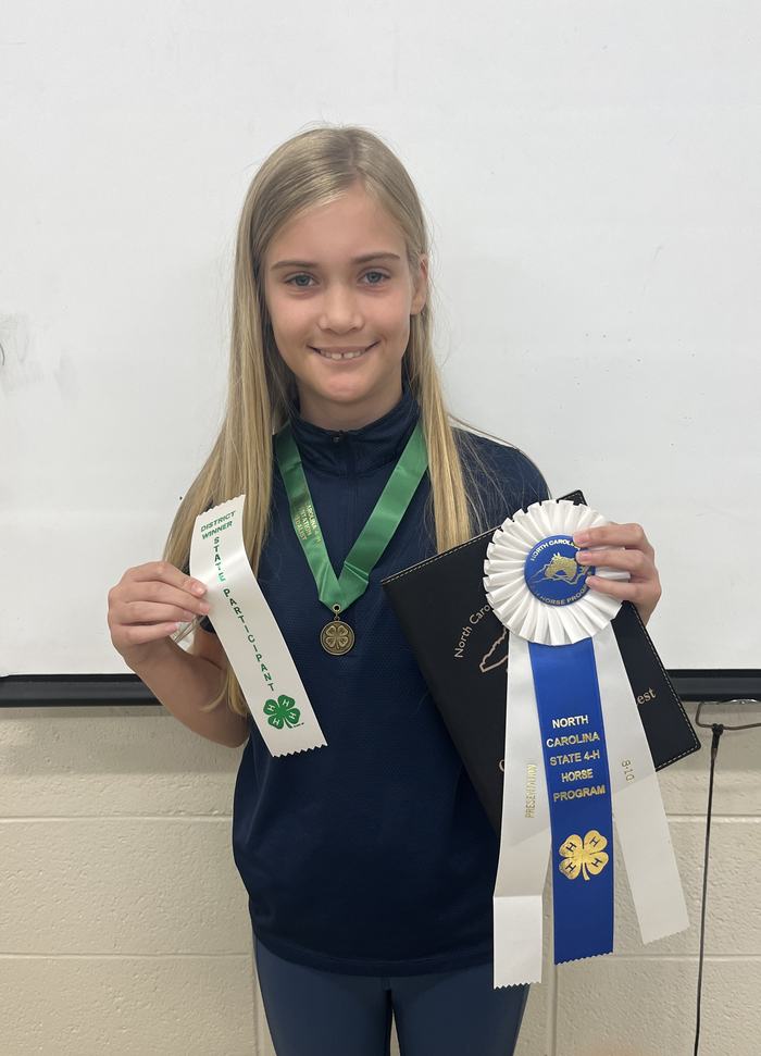 Girl holding medal and ribbons, one ribbon reads "NORTH CAROLINA STATE 4-H HORSE PROGRAM"