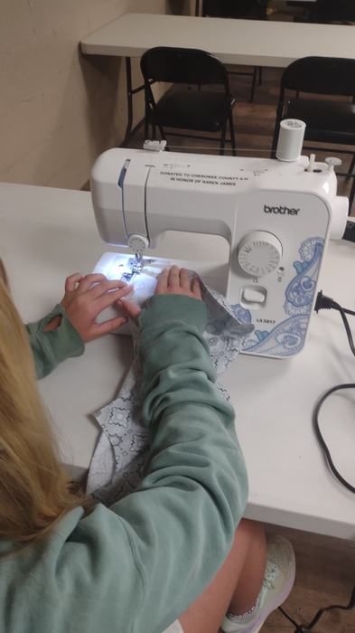 A girl sews with a machine at a table.