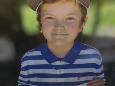 Child wearing cap and blue striped polo holding two award ribbons.