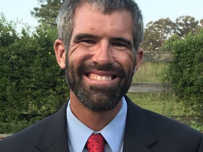A man in a suit and tie smiles near a field.