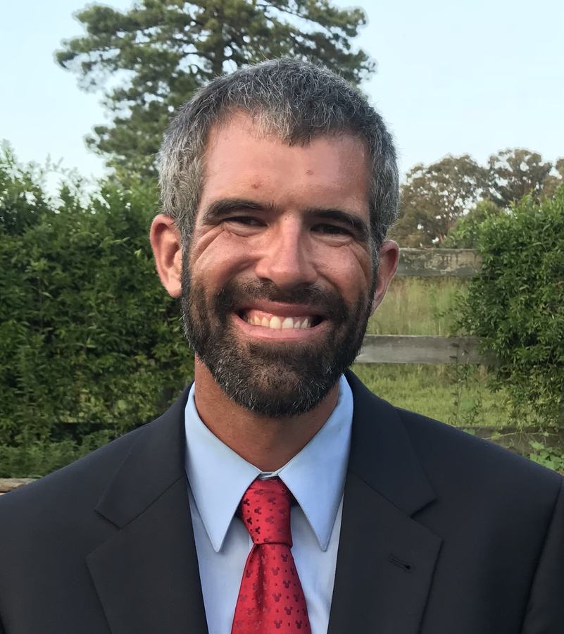 A man in a suit and tie smiles near a field.