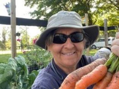 Person wearing hat and sunglasses holding a bunch of freshly harvested carrots in a garden