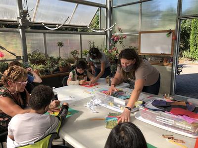Adults and children making paper crafts at a long table inside a greenhouse