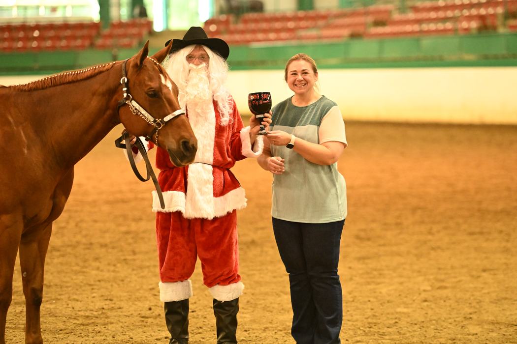 Person in Santa costume holding a horse's reins beside woman holding a trophy in arena