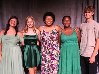 Five teenagers standing side by side facing camera, dressed for an event