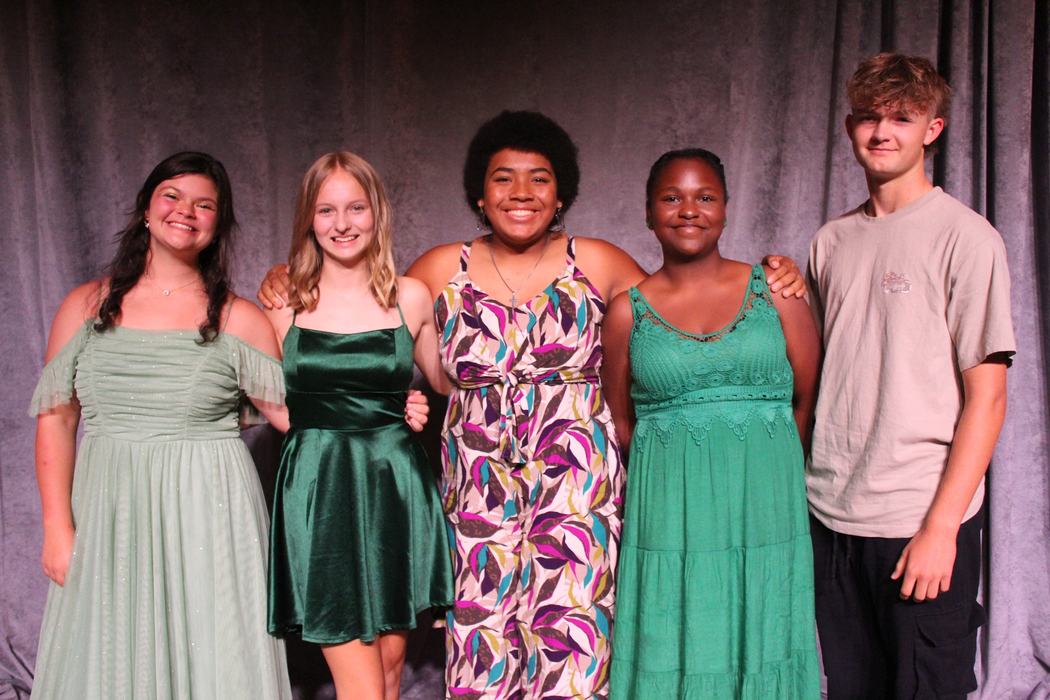 Kids dressed for an event pose together in front of a curtain.