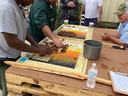 Five men sorting nuts on boards atop stacked wooden pallets outside a metal building