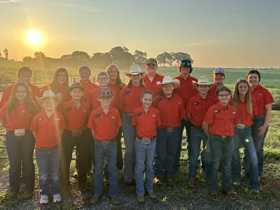 Group of youth in red shirts and cowboy hats standing in a field at sunrise.