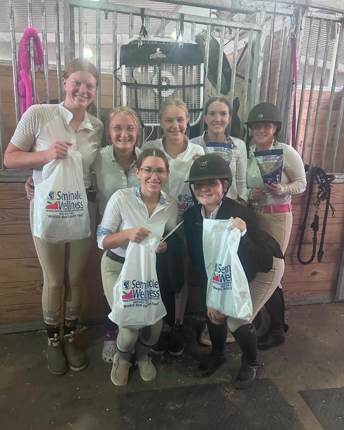 Seven equestrians in a stable holding bags labeled "Seminole Wellness"