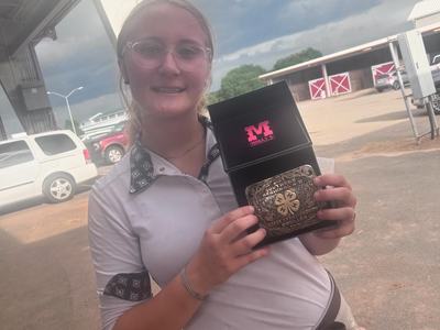 Person holding open box with pink "M" logo and an engraved 4-H belt buckle.