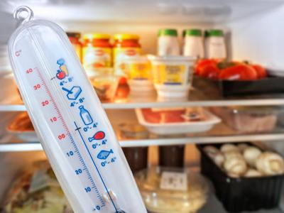 Thermometer in front of open fridge / refrigerator filled with food in kitchen