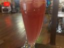 Tall boot-shaped glass with pink fizzy drink and ice on a bar table