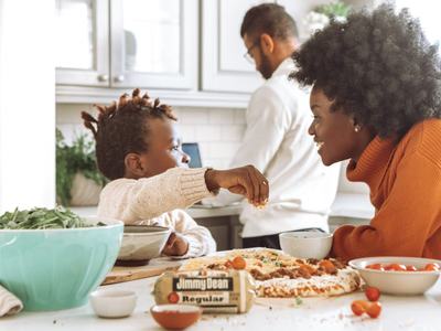 Child sprinkling pizza toppings while adult watches; "Jimmy Dean Regular" package and "Recipes"