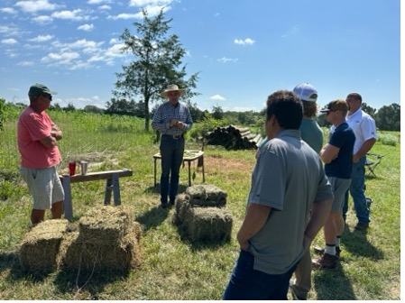 A group of men stand around small bales of hay.
