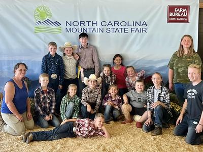 Group of children and adults posing under "North Carolina Mountain State Fair" banner