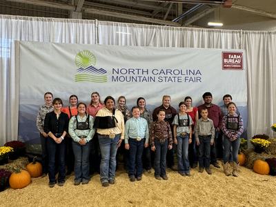 Group of people standing in front of a banner reading "North Carolina Mountain State Fair."