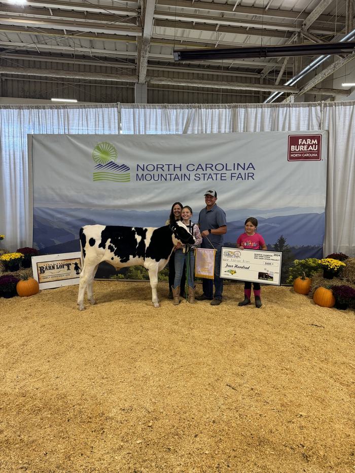 Family with prize cow, ribbon and check in front of North Carolina Mountain State Fair banner