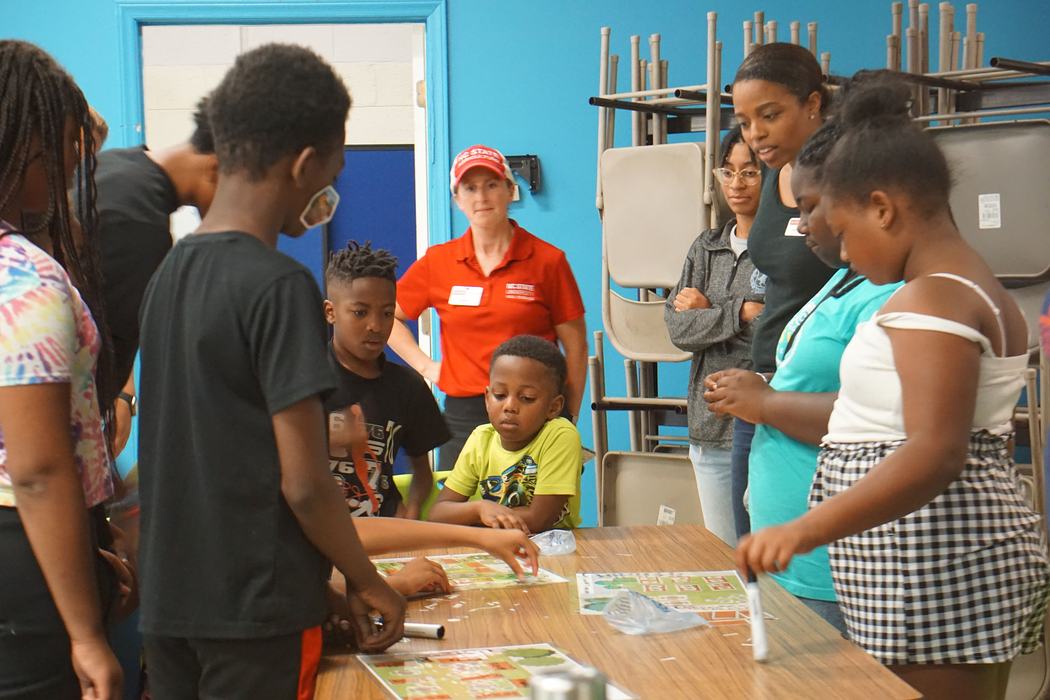 Children and adults gathered around a table assembling game boards and activity sheets