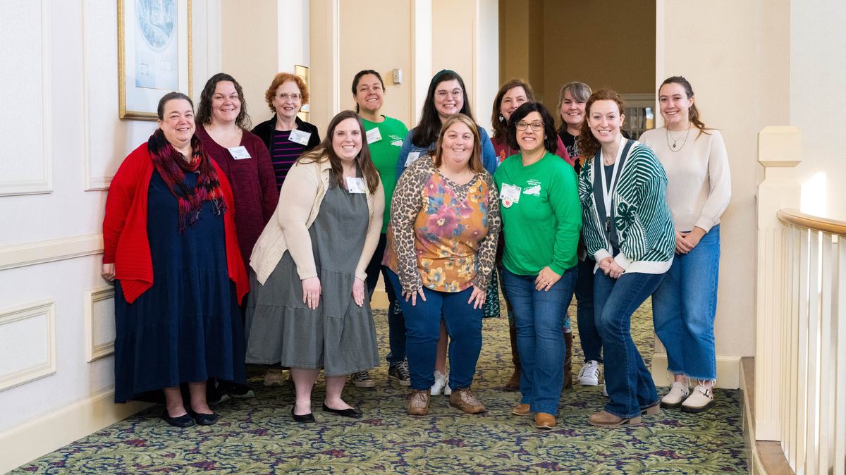 Thirteen women standing in a hallway posing for a group photo