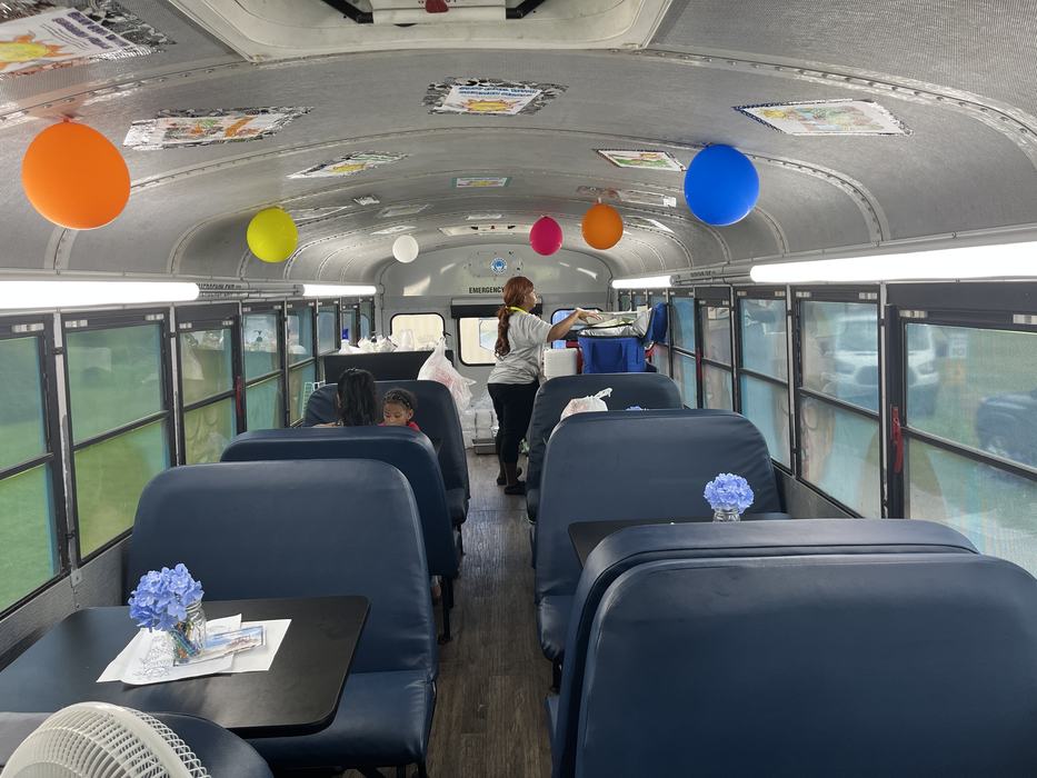 Converted bus interior with tables and balloons; woman arranging supplies at rear