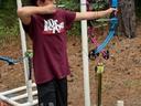 Boy wearing "Dr Pepper" shirt draws a blue recurve bow at an outdoor archery setup