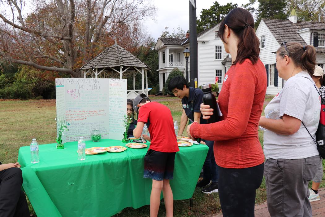 Outdoor table with "Cyberbullying & Bullying" display board and people interacting