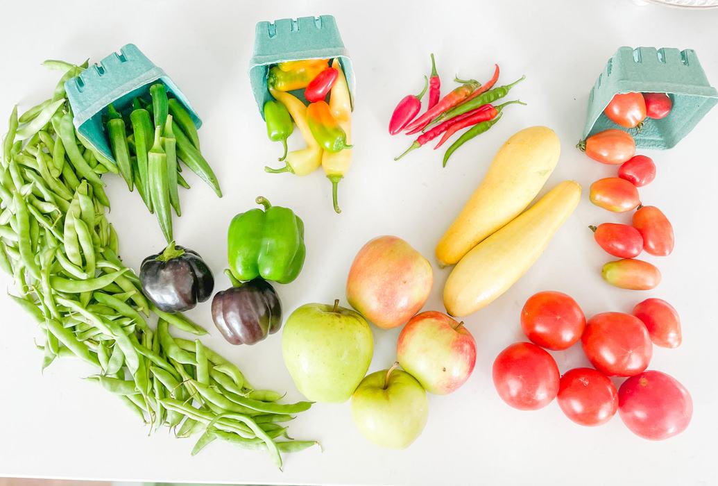 Assorted produce on white table: green beans, okra, peppers, apples, squash, tomatoes