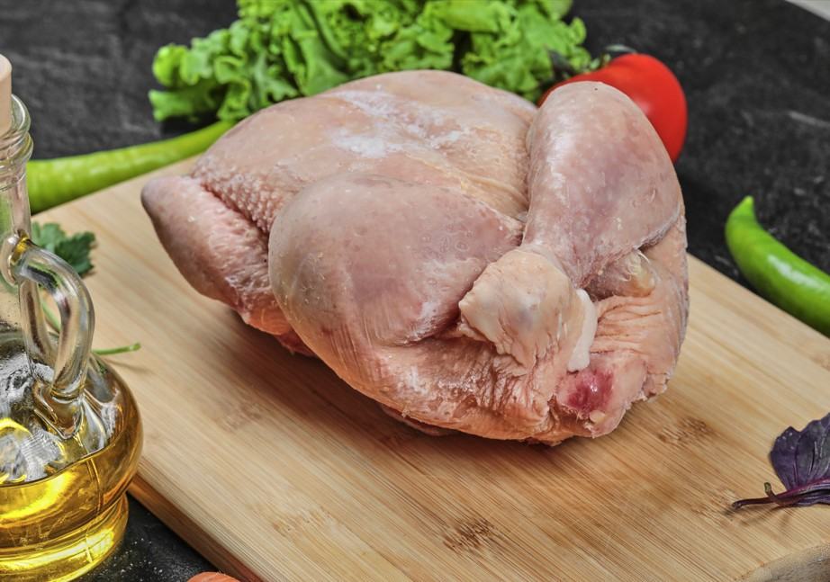 Raw whole chicken placed on wooden cutting board with oil bottle and vegetables