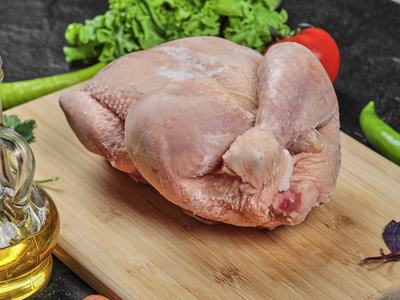 Raw whole chicken placed on wooden cutting board with oil bottle and vegetables