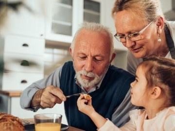 Older man and woman with young girl at breakfast; man feeds girl a bite.