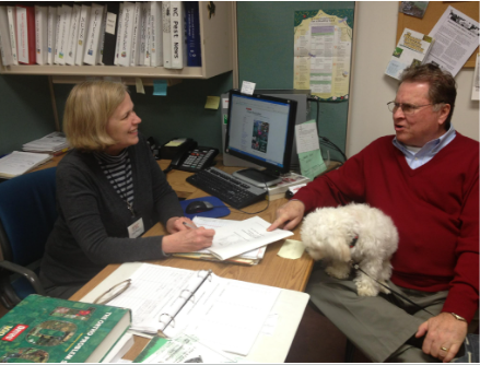 A woman at a desk answers a mans questions.