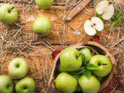 several green apples lying on a wooden table covered in straw