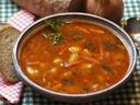 Bowl of tomato vegetable soup with parsley, served with bread slices and a spoon
