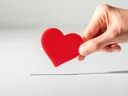 Hand inserting a red heart token into a narrow slot on a white surface