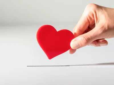 Hand inserting a red heart token into a narrow slot on a white surface