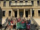Group of students on stone steps holding banner "Perrotis College Study Abroad" and NC State flag