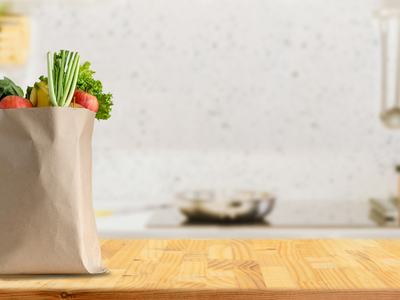A brown paper grocery bag filled with fresh produce on a kitchen countertop.