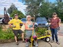 Three gardeners standing by a yellow cart of pulled plants and tools, one shirt reads "Stop Litter"