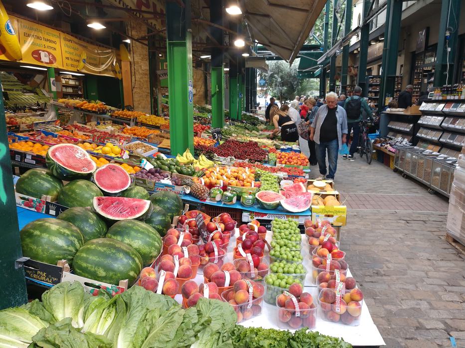 Outdoor market produce stall with watermelons, peaches, grapes and shoppers