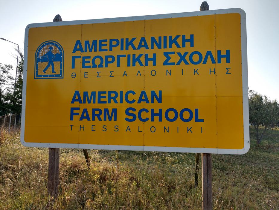 Yellow sign reading "AMERICAN FARM SCHOOL THESSALONIKI" with Greek text above
