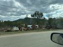 Pile of uprooted trees and debris with damaged cars by roadside, water tower behind