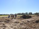 Group of seven people walking across cleared field with piles of uprooted logs and stumps.