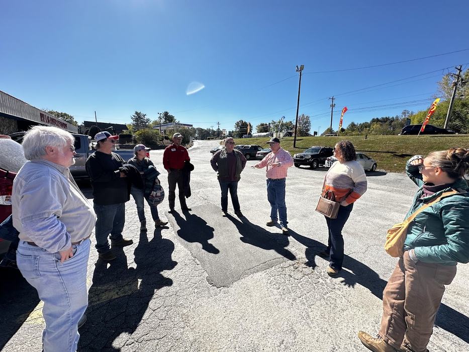 Group of people standing in a sunny parking lot, one person gesturing while others listen