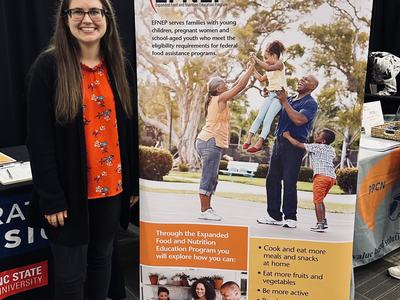 Woman standing beside EFNEP banner displaying family nutrition program information